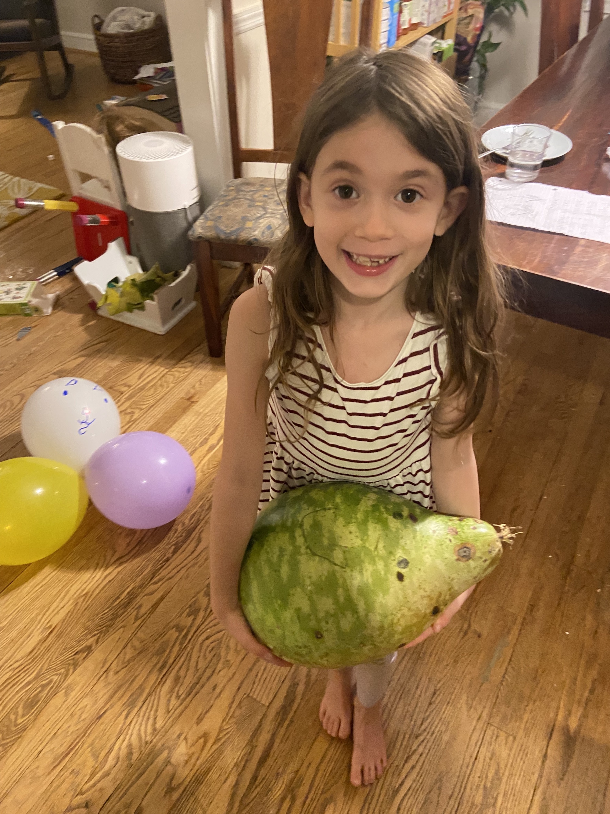 A young girl with a big smile, Eleanor, holds a green gourd–it's bigger than her head!